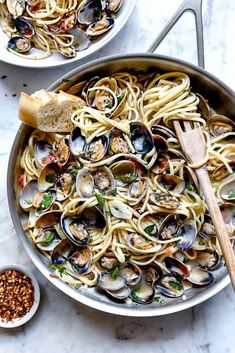 two pans filled with pasta and clams on top of a marble countertop