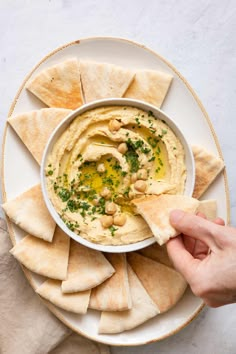 hummus and pita chips on a plate with a hand dipping them into the dip