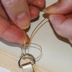 two hands are working on a piece of gold wire that is attached to a pair of scissors