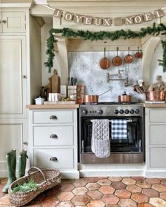 a kitchen decorated for christmas with greenery and copper pots on the stove, pot racks above