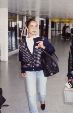 two women are walking through an airport carrying their luggage and looking at the camera man