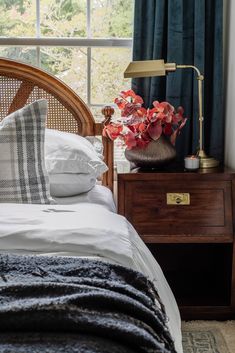 a bed with pillows and blankets on top of it next to a night stand in front of a window