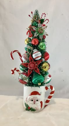 a small christmas tree in a cup with candy canes and ornaments on it's sides