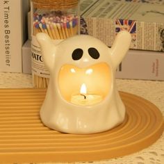 a small white candle holder with a lit candle in the shape of a ghost next to some books