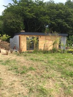 a small shed sitting on top of a grass covered field next to trees and bushes