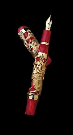 a red and gold fountain pen sitting on top of a black surface with an ornate design