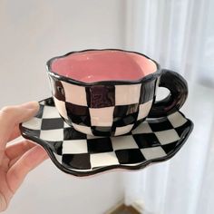 a hand holding a black and white checkered coffee cup with saucer on it