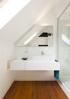 a white bathroom with a skylight above the sink and wooden floors in front of it