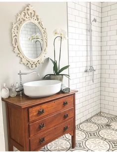 a white sink sitting on top of a wooden dresser next to a bath room shower