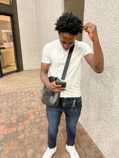 a young man is looking at his cell phone while standing on the side walk in front of a building