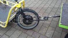 a yellow bike parked on the side of a road next to a green cart with wheels