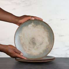 two hands holding a dirty plate on top of a black tablecloth covered surface with white marble walls in the background