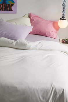 a bed with white sheets and pink pillows