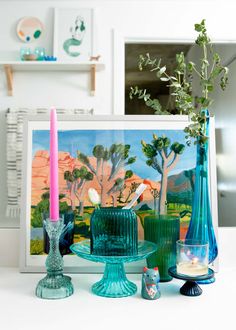 a table topped with vases and candles next to a painting on top of a wall