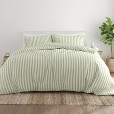 a green and white striped comforter set on a bed with a plant in the corner