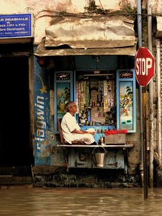 a man sitting at a table in front of a store on the side of a street