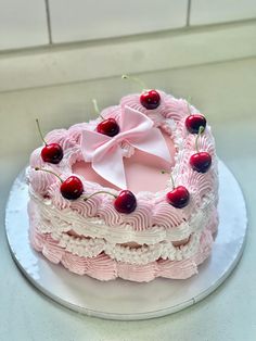 a pink cake with cherries on it and a bow around the top is sitting on a plate