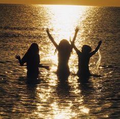 three people standing in the water with their arms up and hands raised above their heads