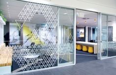 an office with glass walls and yellow stools in the center, along with large windows that have geometric designs on them