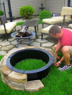 a man kneeling down next to a fire pit in the middle of a grass covered yard