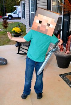 a young boy in a minecraft costume holding a baseball bat and wearing a box on his head