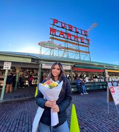 a woman holding a bouquet of flowers standing in front of a sign that reads public market