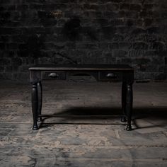 an old black desk with two drawers in front of a brick wall and stone floor