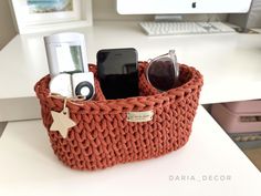 an orange knitted basket with cell phones and other items in it sitting on a desk