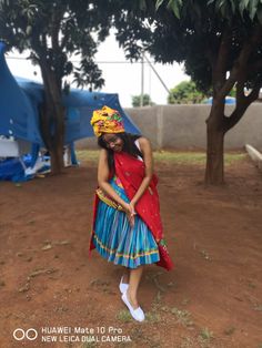 a woman wearing a colorful dress and headdress standing in front of a tree