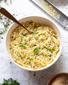 a white bowl filled with pasta and parsley on top of a counter next to a grater