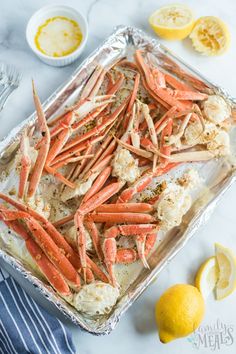 cooked crab legs and cauliflower in a baking pan with lemons on the side