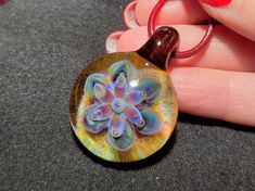 a hand holding a glass pendant with a flower design on it's back end