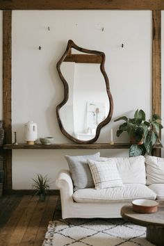 a living room with a couch, mirror and potted plant on the wall in front of it