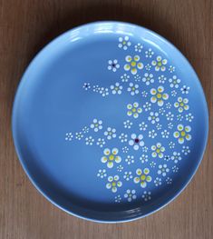 a blue plate with yellow and white flowers on it sitting on a wooden table top