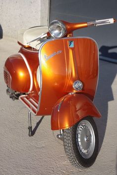 an orange motor scooter parked on the side of a road next to a building