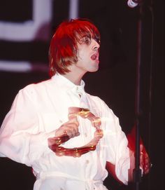 a man with red hair wearing a white shirt and holding a gold snake around his neck