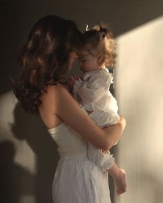 a woman holding a baby in her arms and looking at the wall with sunlight coming through it