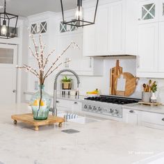 a kitchen with white cabinets and marble counter tops, an island in the middle is surrounded by hanging lights