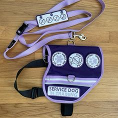 a purple service dog bag on a wooden floor with two lanyard tags attached to it