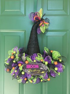 a purple and green halloween wreath hanging on a door with the word booom painted on it