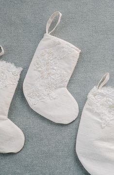 three white christmas stockings with lace and bows hanging from the handles on a gray background