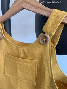 the back of a yellow dress hanging on a wooden hanger next to a black chair