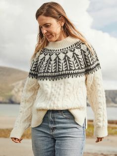 a woman walking on the beach wearing a sweater and jeans