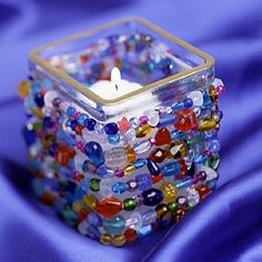 a candle is sitting in a glass container with beads on it's sides and sits on a blue fabric