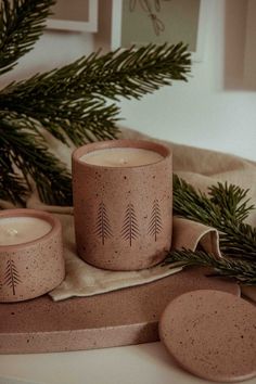 two candles sitting on top of a table next to pine branches