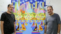 two men standing next to each other in front of a colorful painting on the wall