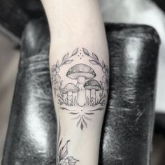 a woman's leg with mushrooms and leaves tattoo on her left arm, next to a black chair