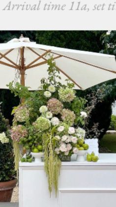 an umbrella that is sitting on top of a white table with flowers and fruit in it