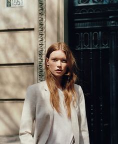 a woman standing in front of a building wearing a white blazer and black pants