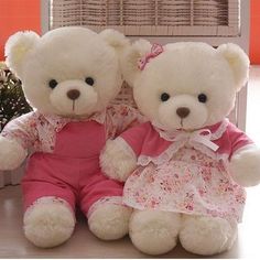 two white teddy bears dressed in pink sitting next to each other on a counter top